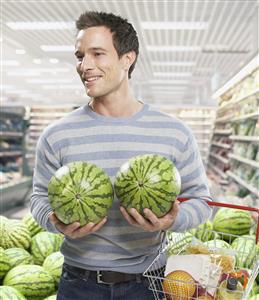 Man grocery shopping holding watermelons