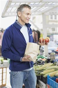 Man grocery shopping holding apples