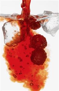 Red liquid pouring into glass with raspberries