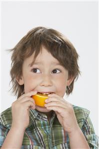 Young boy indoors eating an orange slice