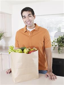 Man in kitchen with grocery bag smiling