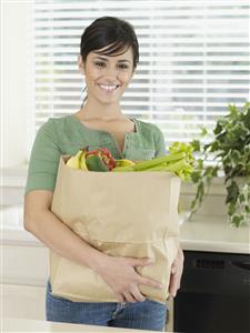 Woman in kitchen holding grocery bag and smiling