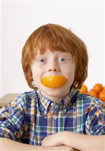 Young boy in kitchen with orange slice in his mouth