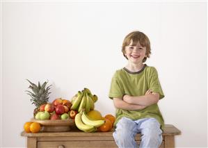 Young boy sitting on kitchen island with assorted fruit smiling