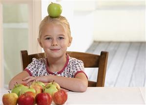 Young girl in kitchen balancing apple on her head smiling