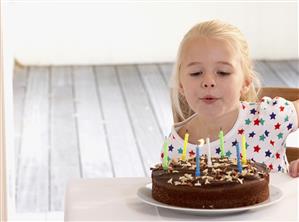 Young girl in kitchen with birthday cake blowing out candles