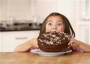 Young girl in kitchen trying to eat an entire cake all at once