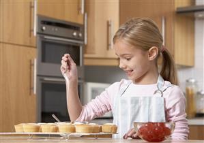 Young girl in kitchen putting icing onto cupcakes and smiling