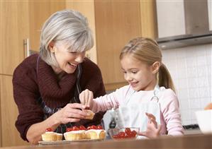 Woman and young girl in kitchen putting cherries onto cupcakes and smiling