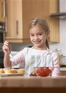 Young girl in kitchen putting icing on cupcakes and smiling