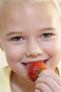 Young girl eating a strawberry and smiling