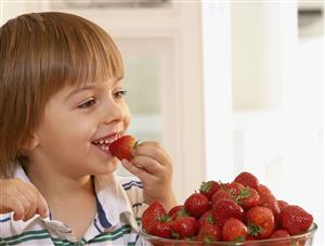 Young boy in kitchen with a bowl of strawberries smiling