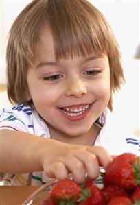 Young boy in kitchen with a bowl of strawberries smiling