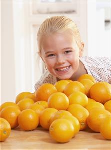 Young girl in kitchen with pile of oranges smiling