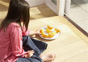 Young girl sitting on kitchen floor eating orange slices