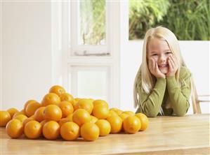 Young girl in kitchen with pile of oranges smiling