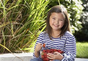 Young girl sitting outdoors with a bowl of strawberries smiling