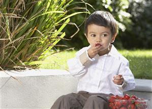 Young boy sitting outdoors with a bowl of strawberries