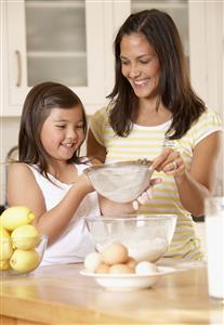 Woman and young girl in kitchen sifting flour into a bowl and smiling