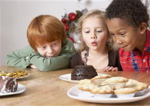 Three young kids in kitchen looking hungrily at desserts on table