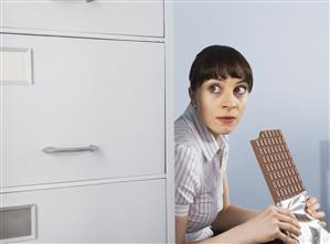 Businesswoman hiding and eating chocolate bar