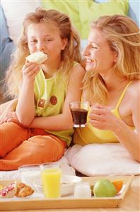 Madre e hija desayunando en la cama.