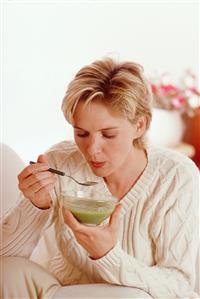 Mujer tomando una sopa de verduras. Viste jersey de manga larga. Primer plano. 