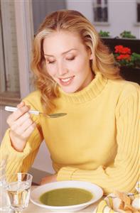 Mujer comiendo pure de verdura. Lleva un jersey amarillo de cuello alto. 