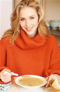 Mujer comiendo sopa. Lleva un jersey rojo de cuello alto. 