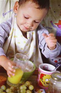 Niño desayunando en la cama un zumo, uvas, cereales, etc. Primer plano.