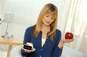 Mujer sospesando en una balanza simbolica, un trozo de pastel y una manzana. Primer plano. 