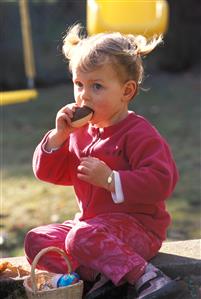 Niña, sentada en el jardin, comiendo un huevo de chocolate. 