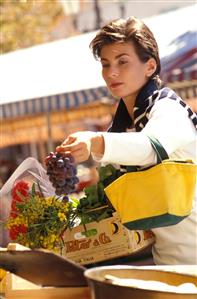 Mujer con un bolso comprando uvas en una tienda de un mercado. 