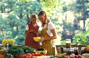 Madre e hija preparando una ensalada en el jardin de casa. La madre tiene un bol en las manos. 