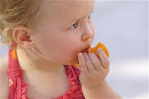 Niña rubia de ojos azules comiendo una fruta.