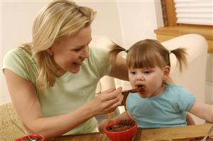 Madre dando de comer a su hija un postre de chocolate. Primer plano.        