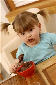 Niña rubia, con coletas, comiendo un postre de chocolate y la cara sucia. Primer plano.        