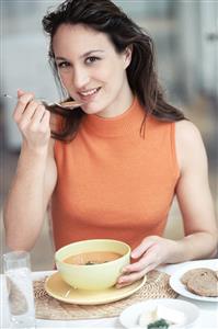 Mujer comiendo una sopa, sonriendo.