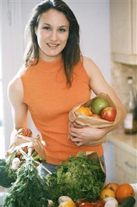 Mujer en la cocina con frutas y verduras, sonriendo. 
