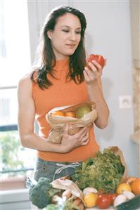 Mujer en la cocina con frutas y verduras, cogiendo y observando una manzana.