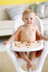 Niño sentado en su sillita comiendo trozos de fruta y ensuciandose.