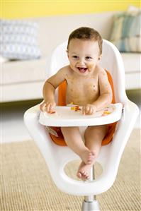 Niño sentado en su sillita comiendo trozos de fruta y ensuciandose.