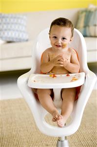 Niño sentado en su sillita comiendo trozos de fruta y ensuciandose.