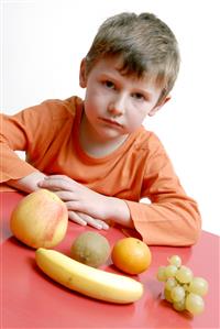 Niño junto a cinco piezas de fruta.