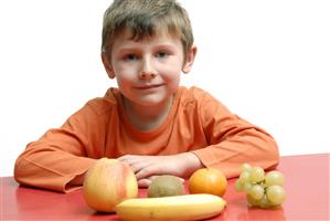 Niño junto a cinco piezas de fruta.