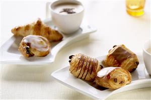 Croissant y pequeñas pastas de hojaldre con chocolate y azucar glass. Tazon de chocolate.