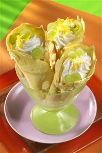 Cucuruchos de bizcocho con uvas y nata en una copa. Receta disponible.
