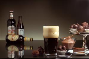 Vaso de cerveza negra con espuma junto a postres de chocolate.